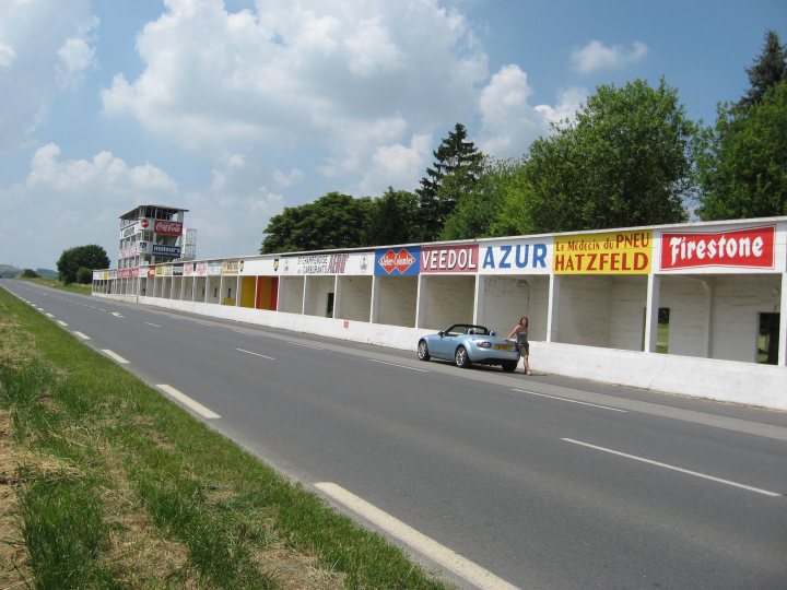 Le Circuit de Reims-Gueux - Page 1 - General Motorsport - PistonHeads - The image captures a serene scene on a highway with signs for rest stops and businesses. A person is making their way along the edge of the road, seemingly unaffected by the closing highway. The sky overhead is a clear blue, dotted with white clouds that add to the beauty of the scene. In the distance, there seems to be an exit for the main freeway, indicating that the highway the person is walking on may be a local or rural route.