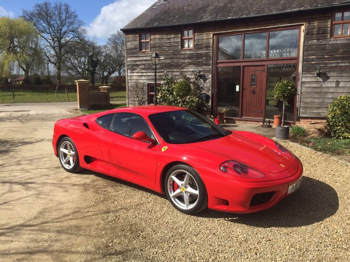 Thanks to Autofficina for transforming my 360  - Page 1 - Ferrari V8 - PistonHeads - The image shows a vibrant red Ferrari parked in front of a wooden house. The car's sleek design and shiny exterior are undoubtedly a highlight. The house behind the car appears to be a charming traditional structure, adding a touch of domestic warmth to the scene. The car is parked on a gravel driveway, and there are plants and shrubs nearby, providing a beautiful contrast to the red of the Ferrari and the timber of the house. The sky above is blue, suggesting a sunny day.