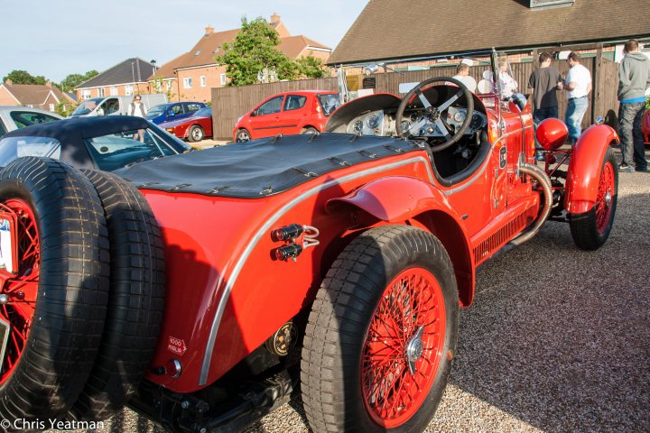 A red and yellow fire truck parked in a parking lot - Pistonheads - This image displays a vibrant red vintage sports car situated in a parking lot. The car features two front wheels prominently in the foreground, and it also has an additional off-road wheel in the back, hinting at its convertible utility. The car's design is characterized by a sleek body and distinctive red rims. The background consists of a variety of euros and other vehicles, signaling a busy setting, possibly a classic car show or a market.