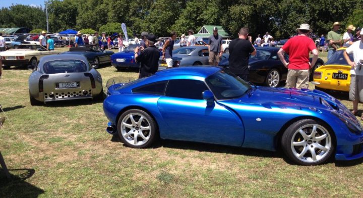 Spotted.... - Page 24 - New Zealand - PistonHeads - The image captures a vibrant car show held on a lush, green field. Multiple sports cars, each boasting a polished exterior, are gracing the field. One of the cars on display is a sleek blue GT. The cars are arranged in no particular order, creating a casual yet exciting atmosphere. Onlookers are scattered around the field, some nearer to the cars while others are at a distance, adding a sense of scale to the scene. The sky overhead appears to be clear and sunny, making for an ideal day for such an event.