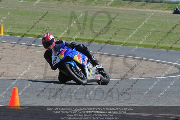 Really fast cars v bikes? - Page 6 - General Gassing - PistonHeads - The image depicts an intense motorcycle racing scene. A series of red and white hydrant-like objects warn about the track's surface, which is made of dirt or a dirt-like material. A red and white motorcycle is taking a sharp turn, slightly up on the back wheel, displaying the skill and balance of the rider. The track curves, suggesting a challenging track design. The environment surrounding the track is relatively flat and appears to be an expansive field or parking lot.