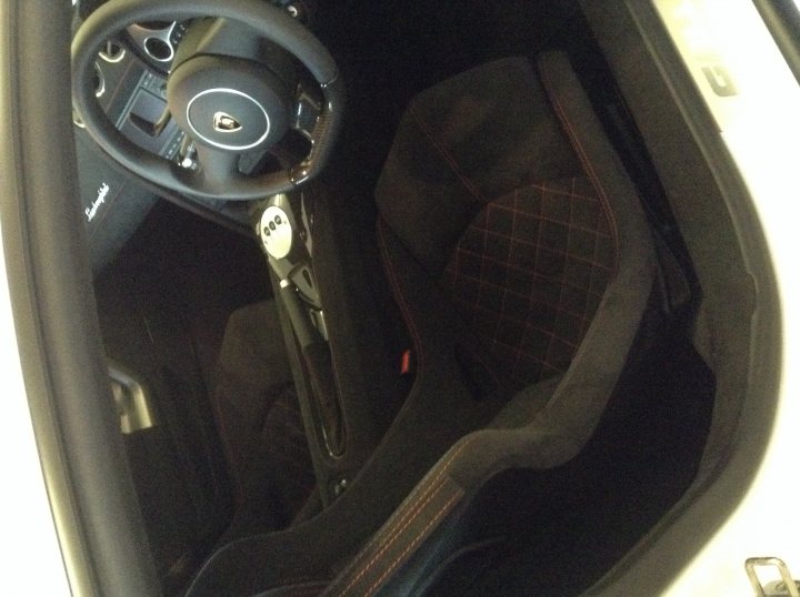 Advice please - Page 1 - Gallardo/Huracan - PistonHeads - The image showcases the inside of a car, focusing on the driver's side and cockpit. The steering wheel, prominently placed, is black with white markings, presumably indicative of the gear shift. Adjacent to the steering wheel, there's a black leather console, which adds to the vehicle's luxurious feel. The seats, upholstered in black leather, are positioned in a way that suggests space for two people. The car's interior features a mix of comfort and functionality, making it an ideal choice for long drives or city commuting. The image provides a glimpse into the car's interior design, highlighting the seat configuration and the positioning of the steering wheel and console.