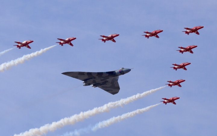 XH558.......... - Page 276 - Boats, Planes & Trains - PistonHeads - The image captures a breathtaking scene of nine fighter jets flying in formation. The jets, painted in a bold mix of red, black, and white, are set against a backdrop of a clear blue sky dotted with wispy clouds. The lead jet divides into two trails of smoke, creating an impressive display below it. The trailing formations emit contrails that streak across the sky, enhancing the spectacle at the backdrop of the clear sky.