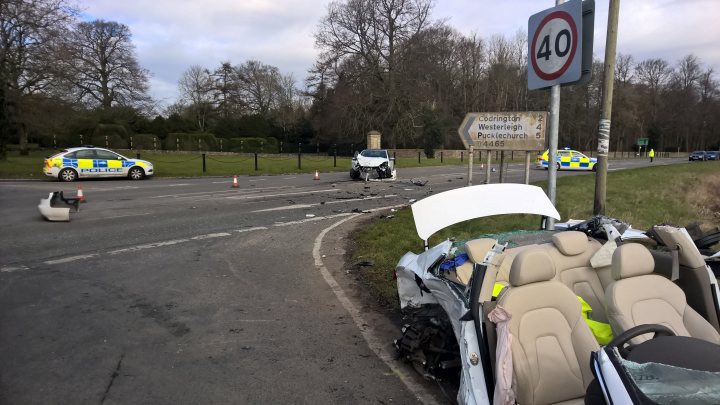 Show us your crash pics!! - Page 206 - General Gassing - PistonHeads - The image shows a roadside scene with a significant amount of debris scattered next to a car. The car appears to be involved in an accident as it is severely damaged and has its rear right side blown open, exposing the interior. In the background, there are a few police cars, indicating that authorities are present at the scene. The scene takes place near a road with some traffic lights visible. The weather is overcast, hinting that the area might have been raining recently.