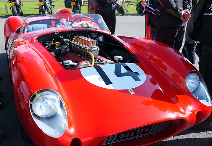 Sunday Meet Anyone? - Page 1 - South West - PistonHeads - The image showcases a sleek, red racing car with the number 14 prominently displayed. It's parked outdoors under a clear blue sky, and several people are gathered around, inspecting the engine. The background reveals other vehicles and some green grass, suggesting a park-like setting. The car's design suggests it's prepared for racing, with various mechanical components visible through its transparent hood. The scene exudes a sense of anticipation and excitement.