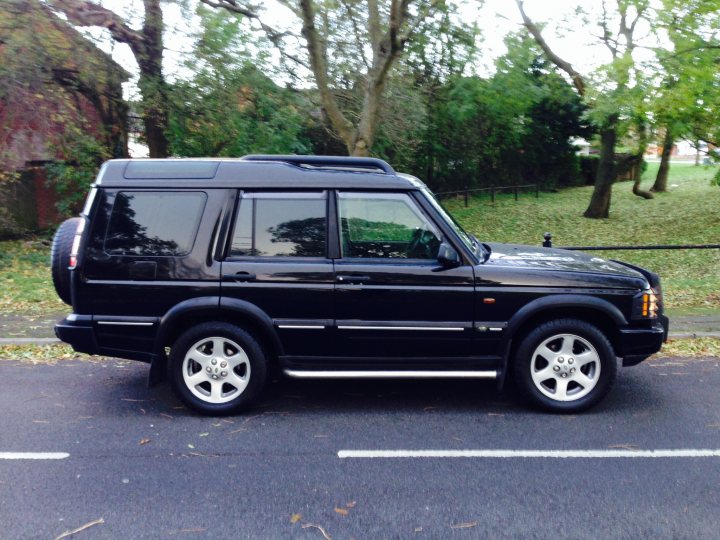 Getting off-road - Page 1 - Off Road - PistonHeads - The image shows a black Range Rover sport utility vehicle. It is parked on a concrete surface with a white line marking the parking spot. The vehicle has a modern design with five doors and five visible windows on the side. The Range Rover features silver needed metal wheels. There is vegetation in the background, with trees and grass indicating an outdoor setting. The sky is not fully visible, suggesting overcast weather conditions.