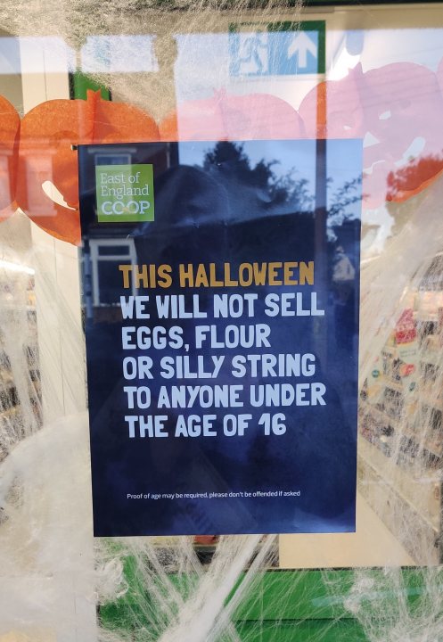 A bit council (Vol 4) - Page 213 - The Lounge - PistonHeads - This image captures a festive scene in a shop window. The window is adorned with Halloween decorations, including jack-o'-lanterns and bats, creating a spooky atmosphere. A sign prominently displayed on the window reads, "This Halloween we will not sell eggs, flour or silly strings to anyone under the age of 16." The text on the sign conveys a clear message from the shop owner about their policy for the season. In the background, there's a glimpse of a bookstore with books on display.