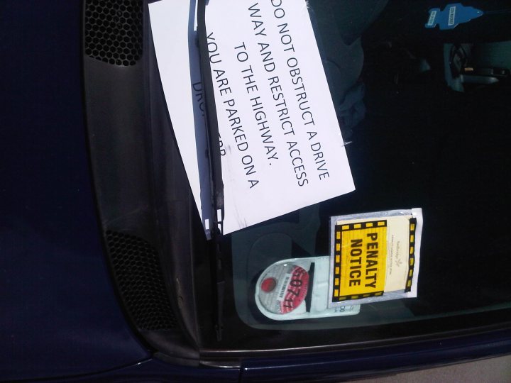 Blocked in on my driveway.  - Page 5 - General Gassing - PistonHeads - The image shows the rear windshield of a car displaying several objects that convey a message. On the screen, there is a white notice affixed which says, "Do not make this restriction disrupt highway access require drive-thru." Positioned just below the notice, there's a yellow and black "Roadblock Ahead" sticker, indicating an obstruction or checkpoint ahead. To the right of this notice is a sensor with a red sticker on it, reading "Radar Speed Monitored." The black windshield provides a backdrop for these notices, making them clearly visible to the driver and other road users.