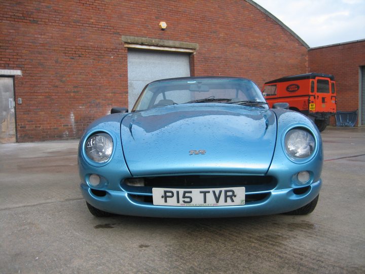 Muncher Resprayed Chimaera Newly Pistonheads Potato - The image shows a small blue vintage car parked on a concrete surface. The vehicle has a distinctive design with a prominent front, round headlights, and a sleek hood. There's also a large front grille and the distinctive "Porsche" badge on the bonnet. In the background, there is a red building, emphasizing the presence of built structures. The car is alone in the foreground, suggesting a quiet setting or possibly a display.