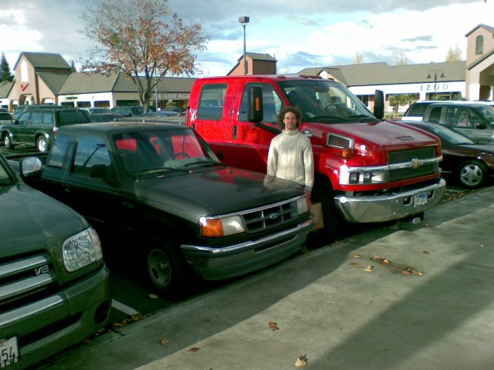 Pistonheads Matter Size - In the parking lot, a woman stands between two vehicles, possibly posing for a photo. A red pickup truck is parked to the left of the woman, and a black SUV is parked to her right. The parking lot is filled with various other cars. The scene suggests an urban setting, and the photo captures a brief moment, perhaps taken for sharing on social media. The woman is the primary focus of the image, standing out against the parked vehicles.