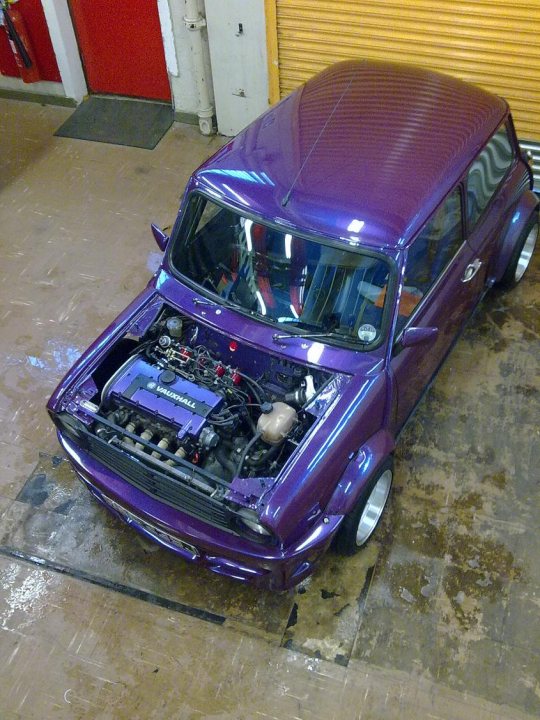 Pistonheads - The image features a classic car with a predominantly purple hue, possibly hinting at modifications or a specific color preference. It appears that the car has seen some mechanical work, as it sits on a garage floor with the hood open, engine exposed, and various parts around. Notably, the car features an upright rear wing and white aftermarket wheels, which adds to its distinctive look. The interior is not visible, but the customized appearance of the car suggests that there might be a unique story attached to it.