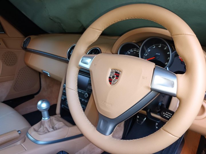 987.2 Boxster 6 speed Gearknob - Page 1 - Boxster/Cayman - PistonHeads UK - The image shows the interior of a car, focusing on the dashboard and the steering wheel. The steering wheel is light brown with a tiny emblem in the center. Above the steering wheel is the dashboard with various instrument clusters including a speedometer. On the left side of the steering wheel, near the center of the dashboard, there is a gear shift. Above the gear shift, one can see the ventilation area of the car's dashboard.