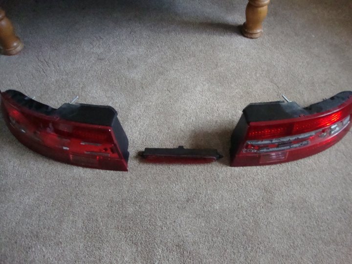 Pistonheads - The image shows two burned-out tail lights against a carpeted floor. An armoire can be seen in the background. The tail lights appear to be from the same vehicle and are likely broken off from the back of the car due to an accident. The carpeting has some wear and there are no signs of any ongoing activity other than the tail lights on the floor.