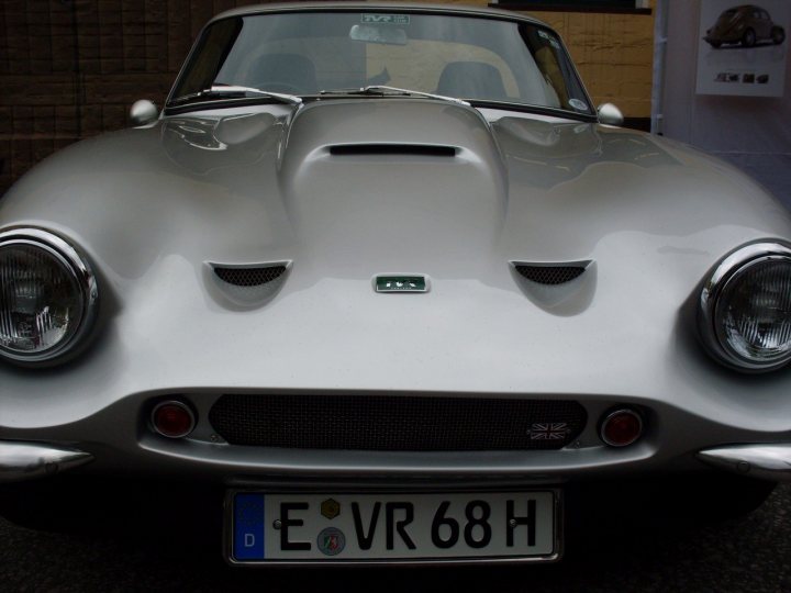 Early TVR Pictures - Page 73 - Classics - PistonHeads - The image showcases a vintage car, an older model with a textured silver exterior that gleams under the light. The car is parked outdoors, with a sleek black wire fence in the background, adding a rustic charm to the scene. The vehicle's distinctive design features a large front grille surrounded by two round headlights, which, together with the black grille, create a striking contrast against the silver body. The license plate is clearly visible and reads "EVR 68 H".