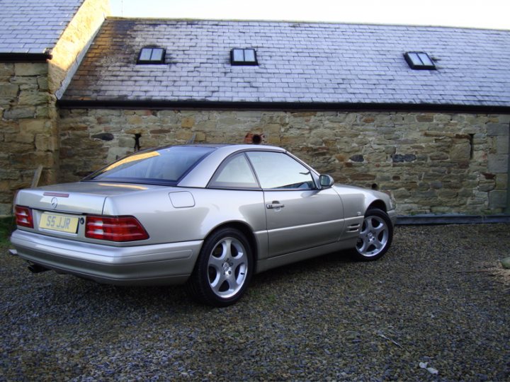 Show us your Mercedes! - Page 78 - Mercedes - PistonHeads - The image depicts a silver passenger car parked on a hard gravel surface adjacent to a building with a stone facade, and a sloped roof with single sleek windows. The car is a European model mid-sized car, likely an executive or family vehicle. Its rims are silver, matching the body, and there is a percentage displayed in the window, possibly indicating the fuel efficiency percentage. Tire pressure gauges are visible with the needle showing the right tire pressure. It appears to be an overcast day, and the sky is pale blue and grey, providing a calm and serene backdrop to the scene.