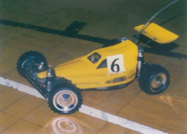 Pistonheads - The image features a vibrant, bright yellow four-wheeled go-kart, which is stationary, placed against a contrasting background. The go-kart has a number "6" prominently displayed, and its position on a surface with white stripes suggests it might be in a garage or on a race track. The backdrop is dark, possibly indicating a tarmac or indoor facility. There's a sense of motionlessness contrasts between the kart and its surroundings, a common theme in racing photography.