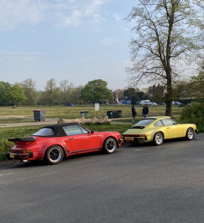 The Curfew XJ-S - V12 manual - Page 21 - Readers' Cars - PistonHeads UK - The image shows two classic cars parked side by side on the roadside. They are a vibrant red convertible and a yellow coupe, both with distinctive aerodynamic designs indicative of 1970s or '80s models. In front of these cars, there is a black trash can and a person standing at some distance. The background features a clear blue sky, suggesting it's a bright day, and several trees are visible in the distance. The overall scene appears to be a sunny day on a street with well-maintained greenery.