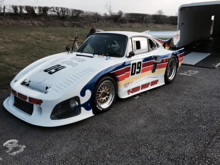 New Sprint Series - Curborough & Throckmorton - Page 1 - UK Club Motorsport - PistonHeads - This image showcases a striking vintage race car parked in a covered area, likely within a transport truck trailer, indicating that it might be in transit. The car is predominantly white with a vibrant blue stripe running down the side. The number 89 is displayed prominently, along with the text "Typical Creep". The wheels feature decorative gold rims, and the hood appears to have sponsorship details. The car's unique aesthetic, reminiscent of classic racing cars, suggests it is a well-maintained piece likely of professional or amateur motorsports, where individual personalities and prestige brands might be represented. The image also includes a portion of the race car driver inside the car, amplifying the human element in this scene. Overall, the image captures a moment of pause amidst speed and competition.