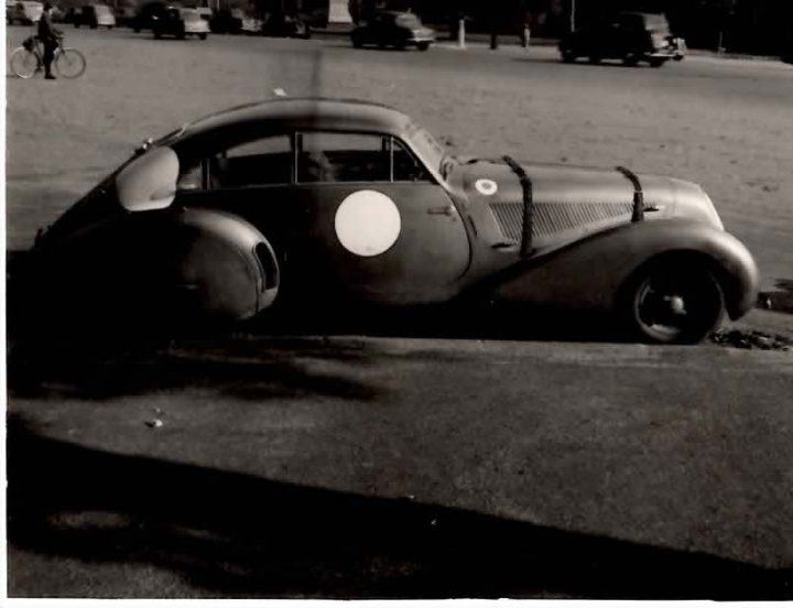 Paulin Fxw Pistonheads Embiricos - The image is a black and white, giving it a vintage feel. It features an old car parked on a street with a person in the distance on a bicycle. The car appears to be in good condition and is reminiscent of classic, possibly early-20th-century automobiles. The street is lined with shops, and there are other cars and trucks in the background, suggesting a busy urban area. The image evokes a sense of nostalgia, harkening back to an earlier era in transportation and architecture.