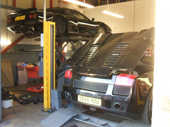 Pistonheads - The image shows an inside garage or workshop setting. There are two sports cars in the image, one on a hoist and the other parked on the floor. The hoist is currently holding the back of the second sports car, possibly for sale, indicating some maintenance or preparation work is being done. The number plates of the sports cars are white and yellow. The environment suggests a professional setting, likely a repair shop or a car enthusiast's own garage.