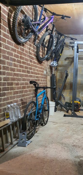 Displaying bikes - Page 1 - Pedal Powered - PistonHeads - The image showcases an indoor space, possibly a garage or storage room, where a variety of bicycles are neatly arranged. There are several bicycles hanging on the brick wall, with their tires and seats facing outwards. On the lower shelf, there's a collection of bikes leaning against it, suggesting an organized setup for storing these vehicles. The room has a distinct industrial feel with its exposed brick walls and concrete floor.