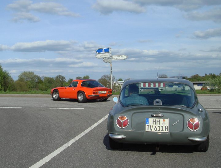 Early TVR Pictures - Page 11 - Classics - PistonHeads - In the image, there are two cars on a three-lane highway with a person in the passenger seat of the green car in front of an orange one. Both are facing away from the camera. The sky is partly cloudy, and the cars are adorned with American license plates.