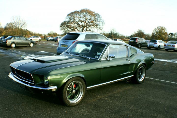 Your Car History In Pictures. - Page 1 - General Gassing - PistonHeads - The image captures a classic green Mustang parked in an empty parking lot under a windy day. The car's metallic finish gleams under the clear blue sky. The Mustang's sleek design and shiny finish stand out prominently against the misty clouds adridting the sky. The parking lot stretches out to a lush green field beyond it, where other cars can be seen resting idle. The scene exudes a sense of tranquility and solitude, with the Mustang being the main focus of the image.