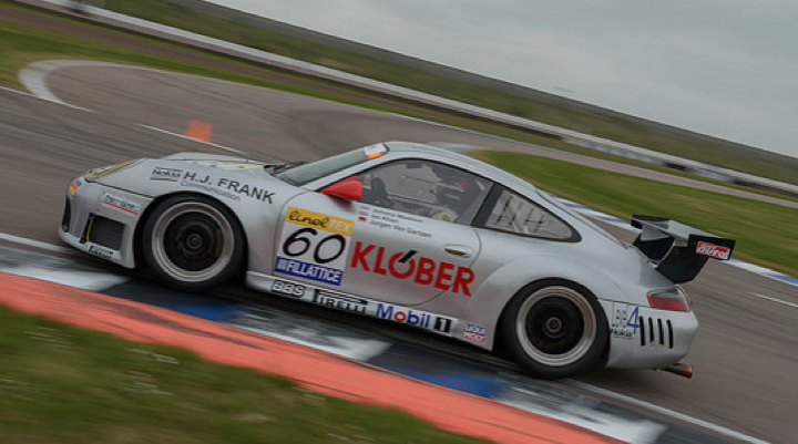 991.2 GT3 reviews out - Page 6 - 911/Carrera GT - PistonHeads - The image captures a thrilling moment on a curvy racing track. A silver Porsche 911, adorned with sponsor names and logos, is in full swing around a corner. The car is marked with the number 60 and the word "K Familie Racing". The track is equipped with orange and blue barriers to ensure the safety of the high-speed racers.