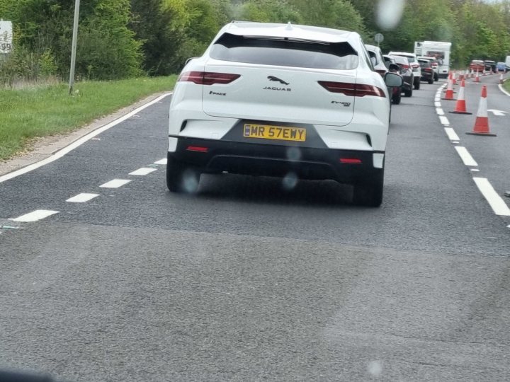 What C124PPY personalised plates have you seen? V01. 3 - Page 359 - General Gassing - PistonHeads UK - The image depicts a scene on a road where a white SUV is traveling. The car has a distinctive license plate with text and numbers, indicating it might be a rental vehicle or have special status. It is driving towards the viewer, captured in motion as it crosses from one side of the road to the other. 

In the foreground, there is a dashboard camera mounted on the front window of another vehicle, capturing the image. The reflection of that car can be seen on the windshield. 

The background shows a clear sky, suggesting good weather conditions at the time the photo was taken. The road appears to be in a rural or semi-rural area with a green landscape visible. The overall setting suggests a typical day on the road, possibly during a journey from one location to another.