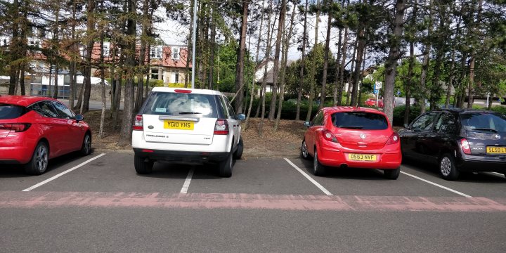 The BAD PARKING thread [vol4] - Page 517 - General Gassing - PistonHeads UK - The image depicts a scene of a parking lot with several cars parked in slots. A prominent feature is the presence of a small, white truck parked in one of the spaces, with its rear facing the camera. The cars vary in color and model, suggesting that this is a public parking area. There are no people visible in the image, and the focus is on the vehicles themselves. The lot appears to be outdoors and possibly near a forested area, given the glimpse of greenery in the background.