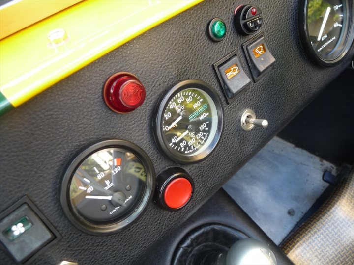 Spent 4 hours cleaning - Page 1 - Caterham - PistonHeads - The image shows a close-up of the driver's side panel of a vehicle. The panel is black with several control buttons that are most likely for the gear, window, and other vehicle functions. There is an orange button indicating a hazard switch. Two gauges are visible: one is an orange button that might be for action or start, and the other is a black gauge, which appears to be the speedometer, but without the full context, the exact function isn't clear. The overall impression is of a control panel for the vehicle's operation.