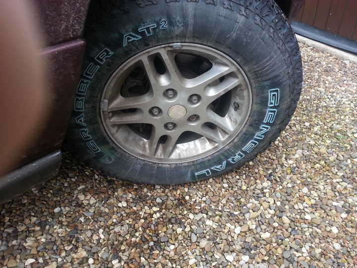 A cat sitting on top of a black car - Pistonheads - The image captures a close up view of a tire on a vehicle, featuring the word "GENERAL" inscribed along its side. The tire is partially covered in dirty gravel, possibly indicating recent off-road use or a driveway setting. The surrounding area is composed of pebbles and rocks, adding a rugged feel to the scene. Due to the angle and quality of the photo, the specific make and model of the vehicle aren't visible from this perspective.