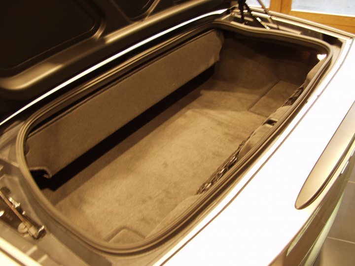 Pistonheads Boring Question - The image features an open car trunk. The trunk liner is visible, revealing a dark grey or black material, possibly a mat. The trunk appears spacious, with a smooth floor and a slightly curved side wall. The rear window of the car can be seen in the reflection, indicating that the trunk is open for viewing. The car is slightly visible in the background, suggesting that the photo may have been taken in a garage or a showroom.