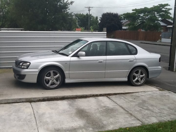 My new RS30 - Page 1 - Subaru - PistonHeads - The image shows a silver-colored sedan parked on the side of a street. Set against the backdrop of a residential area, the car appears to be a four-door sedan. It's parked in front of a white structure that might be a garage or covered area. The sidewalk where the car is parked is adjacent to a neatly trimmed lawn and houses visible in the background. The weather seems to be overcast, suggesting it might be a cool or cloudy day. The car is stationary, with no visible motion. There are no people or animals in the immediate vicinity of the car. The photo captures a typical daytime scene in a residential neighborhood.