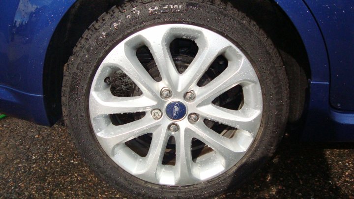 Aint Wait Pistonheads Corsa Currys - The image showcases a close-up view of a single vehicle's tire. The tire is predominantly made up of black and gray rubber, with a white hubcap featuring five silver bolts arranged in a diamond pattern. The tread of the tire with its grooves and sipes is clearly visible against the darker background of the tire's sidewall. A small blue logo is also discernible on the hubcap, adding a touch of color to the otherwise monochrome design.