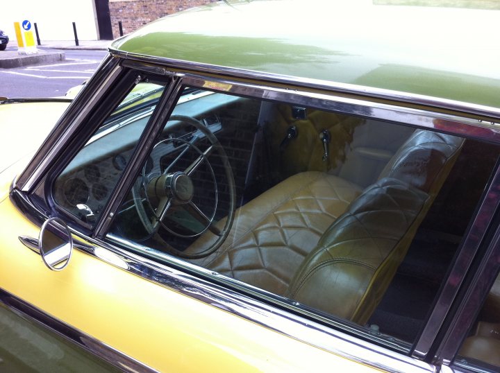 Pistonheads - The image captures the interior of an old, yellow car, focusing on the driver's seat. The vintage car's interior is richly detailed with a leather upholstery that exudes an air of elegance. The car seat, which is visible, is made of leather, adding to the car's vintage charm. The car's steering wheel, also featuring leather details, forms the central element of the image, drawing attention with its placement. Finally, the tinted windows and sunroof are open, suggesting the car is parked in a public area, as indicated by the street view at the bottom of the image.