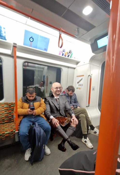 Pistonheads - The image is a candid photograph taken inside a subway car. A man, possibly of East Asian descent, wearing a suit and tie is seated on the bench facing the camera with a slight smile. He appears to be engaged in a conversation or looking at something off-camera. The subway interior has orange seats and a sign is visible above him indicating that the train is on a standstill. There are additional passengers present, all seemingly absorbed in their own activities. The overall atmosphere of the image suggests a typical day of public transportation with people minding their business.