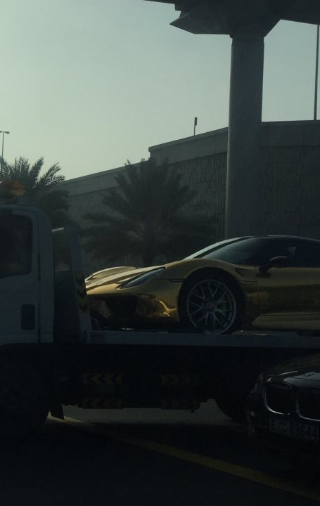 Middle East spotted thread - Page 77 - Middle East - PistonHeads - The image shows a scene of a tow truck in action. The tow truck, painted in a striking blue with a white roof, is towing a highly polished gold car. The gold car is flatbed topped, signifying that it may be of significant worth or value. The backdrop of the scene is a gray building with a parking area, and palm trees can be seen in the distance, suggesting a tropical or subtropical location. The tow truck is taking the car to a location that is not visible in the image. The actions depict the transport of the gold car using the tow truck.