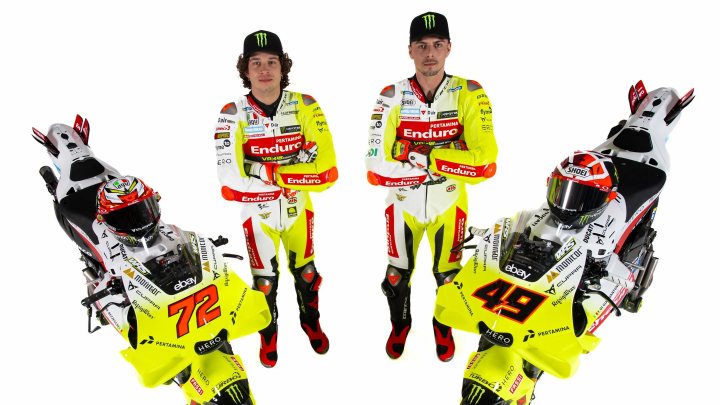 Pistonheads - This image features three individuals standing in front of a backdrop with a sports theme. They are dressed in racing attire, suggesting they are related to motorsports or racing teams. The person on the left appears to be a driver, identifiable by the racing suit and helmet, which is not fully visible. In the center, there's another individual wearing a similar racing suit but with more of their body and face exposed. On the right side, there's a person who seems to be a team member or mechanic, indicated by the attire that includes a tool belt and overalls. They all have their arms outstretched as if posing for the photo. There are no visible texts or logos in the image. The style of the image is promotional, likely meant for marketing purposes.