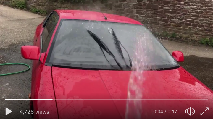 Awkward design details on production cars - Page 28 - General Gassing - PistonHeads - The image captures a vivid scene on a street. A bright red car sits in the center of the frame, its glossy hood and body gleaming. The sun is highly reflective off its surface, suggesting a clear day. A large plume of water is seen erupting from the car's hood, creating a circle of water that matches the car's vibrant color. This water spout is the main action in the photo, drawing the viewer's attention. In essence, the car and its flowing water surface serve as the dominant elements in the picture.