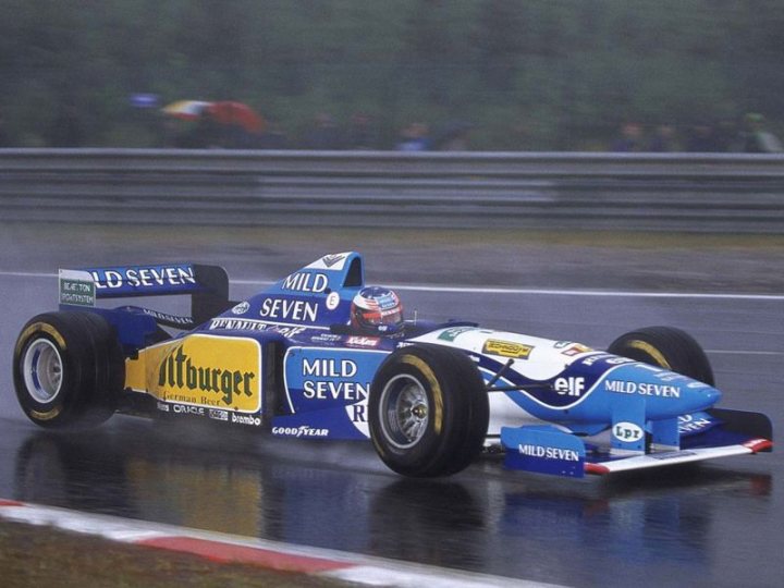 Sauber C34 - Page 1 - Formula 1 - PistonHeads - This image captures a thrilling moment in a Formula One race. The driver is seen using a steering wheel, a crucial component of the racing experience. The car is a striking blue, white, and yellow, adding to the excitement of the race. The background showcases the race circuit, complete with metal barriers, aerial grandstands, and many spectators who have come to witness the high-speed action. The focus is clearly on the racing car, illustrating the intensity and competitive atmosphere of the event.