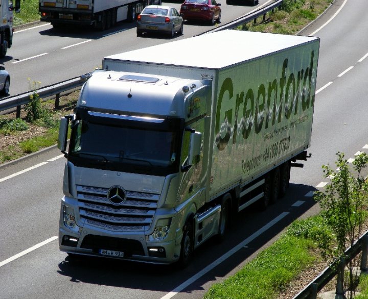 A truck is parked on the side of the road - Pistonheads - The image captures a dynamic scene on a highway. At the center of the frame is a **silver semi-truck** emblazoned with the text "GREENFORD" across its side, indicating the name of the company it belongs to. The truck is in motion, traveling from the left side of the image towards the right.

In the background, the highway bustles with other vehicles, including **cars** and **trucks**. The presence of these vehicles adds a sense of activity and movement to the scene.

The highway itself is a major feature in the image, stretching out in both directions. This suggests that the highway is a significant transportation route.

The landscape on either side of the highway is not clearly visible, but hints of **trees** and possibly a mountain can be discerned, lending a touch of nature to the otherwise industrial scene.