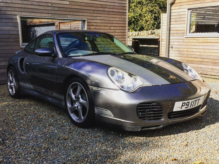 The Beautiful Porsche Picture - Page 6 - Porsche General - PistonHeads - The image showcases a sleek, blue Porsche sports car, parked on a gravel driveway. The car is facing slightly to the left, with the notable logo of the Porsche on the front grille. The surrounding environment includes wooden buildings in the background, adding to the overall scenic setting. The car's position and the placement of the buildings suggest this could be a private residential area or perhaps a luxury vacation spot.