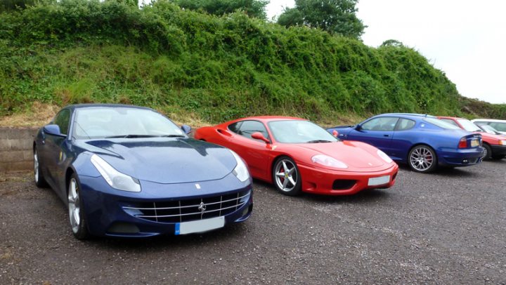 A car parked on the side of the road - Pistonheads - The image showcases a trio of sports cars parked in a lot adorned with a backdrop of lush greenery. The cars are arranged in a line, with the blue car situated on the left side of the image, the red one in the center, and the black one towards the right. The cars display prominent, emblematic logos on their grills, adding to their sleek and sporty designs. The surrounding natural elements contrast with the man-made precision of the vehicles, hinting at the harmony between technology and nature.