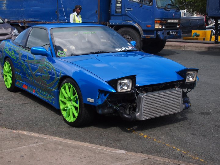 Pistonheads - In the image, there's an older model blue sports car parked on a street next to a blue truck. The car is positioned slightly behind the truck, both vehicles occupying their respective parking spots. The car's design and the large side mirrors of the truck are the most noticeable features of these vehicles. The overall scene suggests a typical day with everyday vehicles on a city street.