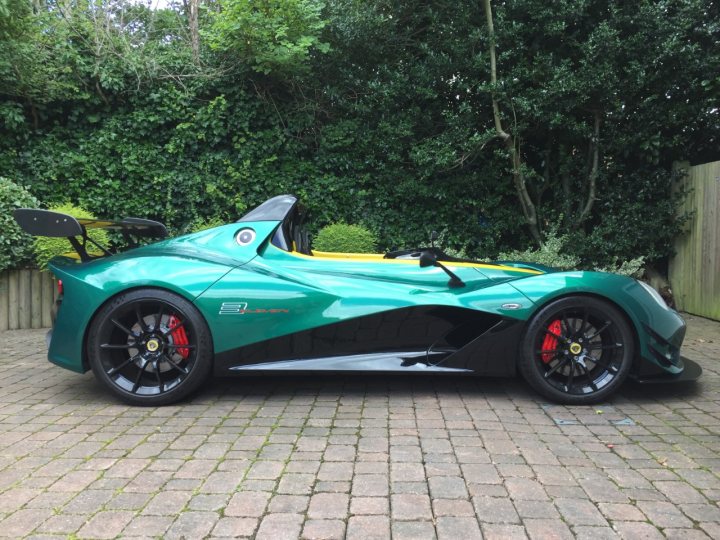 Lotus 3 Eleven - Page 8 - Readers' Cars - PistonHeads - The image shows a sleek, open-top sports car parked on a brick driveway. The car is painted in a vibrant green hue and has what appears to be a black and red striped pattern on the hood. Large air intakes are visible on the sides near the rear, and the overall design is aerodynamically modern, suggesting high performance capabilities. The car is situated in a residential area with well-maintained hedges in the background. There are no visible texts or brands on the car. The style of the photo is realistic with a slight focus bias towards the front of the vehicle, enhancing its dynamic appearance.