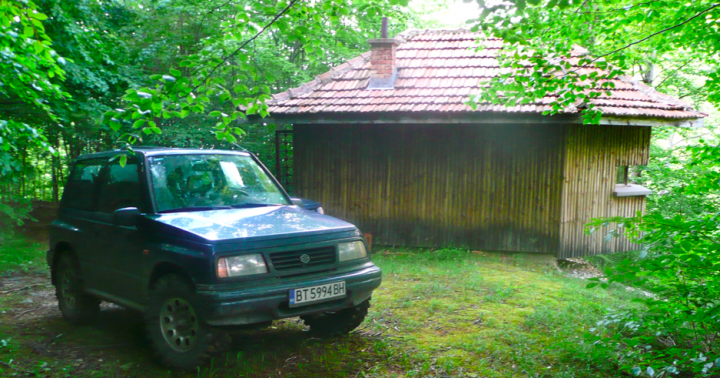 Little overnight trip to the Balkan range - Page 1 - Off Road - PistonHeads - This image depicts a serene outdoor scene. A dark green SUV is parked on a grassy area, framed by trees. In the background, there is a quaint beige and gray hut with a tiled roof. The hut appears to be a small shed or possibly even an animal enclosure. The setting suggests a rural or suburban environment, where the man-made structures coexist harmoniously with the natural surrounding.