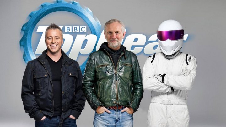 Top Gear 2016 Official  TV show thread *contains spoilers* - Page 1 - TV, Film & Radio - PistonHeads - The image is a promotional picture that features three individuals, presumably associated with the 'BBC Top Gear' program, each standing on the word 'TOP GEAR' against a light background. In the center, there is a man with a slightly messy hairstyle wearing an olive green leather jacket and blue jeans. His expression is lighthearted with a lopsided grin, and he is looking slightly away from the camera with his eyes partially closed. To the left, another man with a clean-shaven head and a beard is wearing a dark jacket and a white shirt. He is smiling and looking directly at the camera with his hands in his pockets. To the right, there is a third man who is wearing white racing attire, complete with a racing suit, white racing shoes, and a white racing helmet with a visor. He is also smiling and looking sideways at the camera with his arms crossed over his chest.