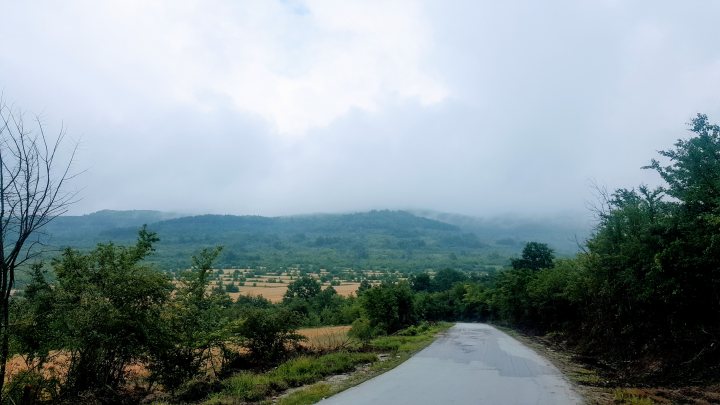 The "Photos From Today's Ride" thread. (Vol. 2) - Page 23 - Pedal Powered - PistonHeads UK - The image is a vertical photograph of an overcast day. It shows a rural landscape with a road that leads towards low-lying mountains or hills. There's a clear boundary between the foreground and the background, where the road meets the natural environment. The sky is filled with gray clouds, suggesting the photo was taken on a cloudy day. In the lower part of the image, there appears to be a watermark or logo, but it's not possible to read or identify the content within this area due to the resolution and angle.