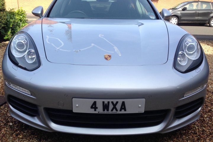 A car is parked on the side of the road - Pistonheads - The image shows a silver-colored sports car with a distinctive design. It is parked on a gravel driveway, facing the camera at an angle that captures its prominent features. Notable features include its sleek hood, which is adorned with a unique, curved white pattern. On the front bumper, there is a registration plate with the letters "4WXA". The car's design suggests a high-end model, indicative of performance and luxury. Its position and the angle at which it is taken give a clear view of its aggressive styling. The drive and the setting evoke a sense of everyday elegance.